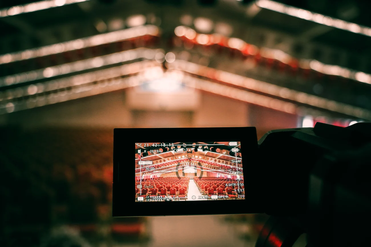 Videokamera vor einer Bühne, mit einem Auditorium auf dem Kameradisplay